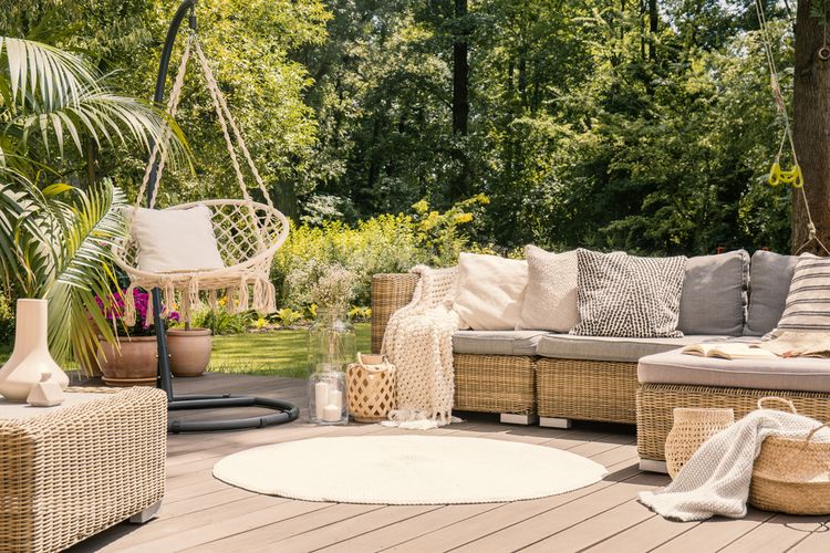 A big terrace with a comfortable leisure sofa with cushions, a table and a string swing in a green garden during sunny vacation.